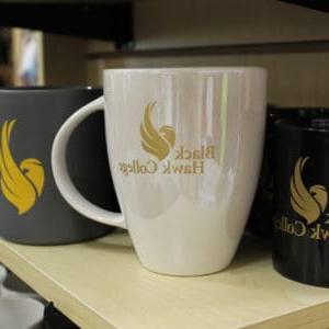 White coffee mug with Black Hawk College logo on a store shelf